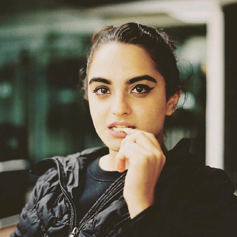 Brinda Gulati - Portrait of a woman with dark hair pulled back, wearing black jacket and eye makeup.