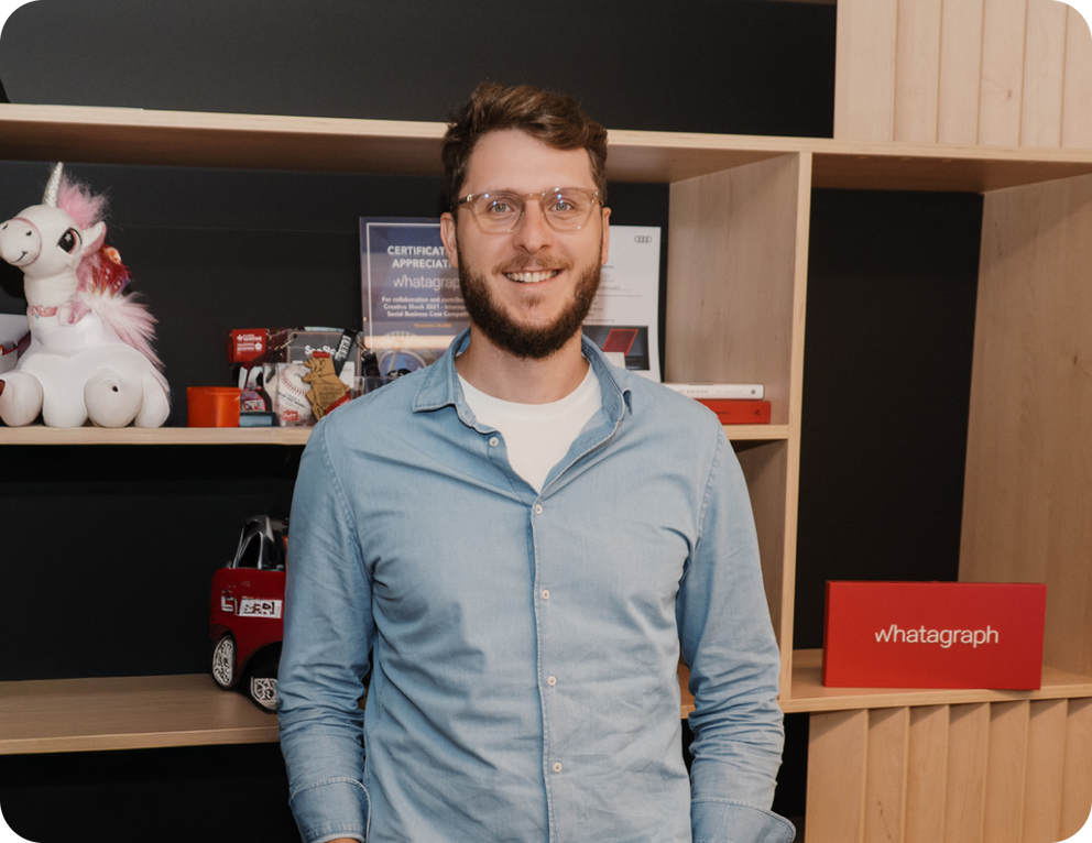 Justas - A man smiling with a shelf filled with items behind him.