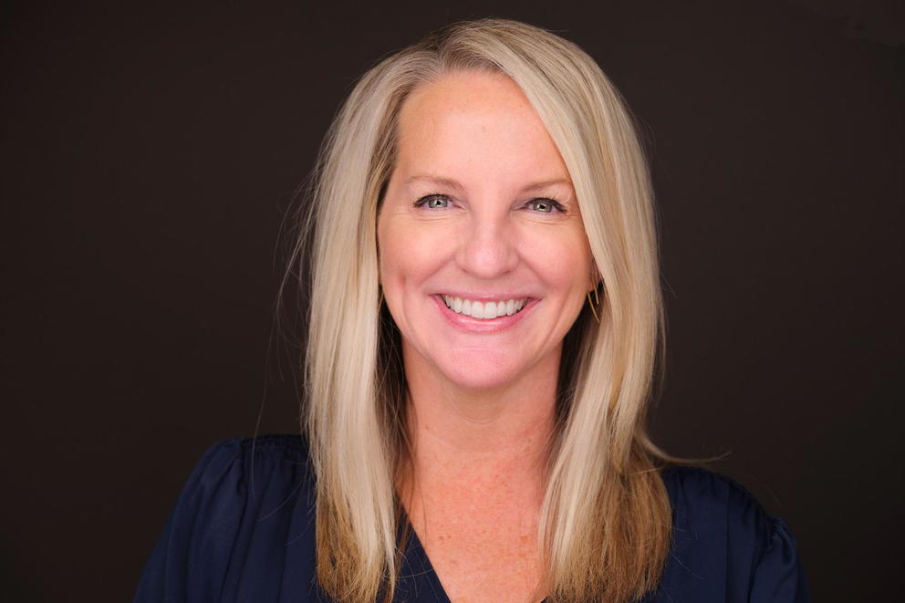 Robin Emiliani - Headshot of a smiling blonde woman with a dark background.